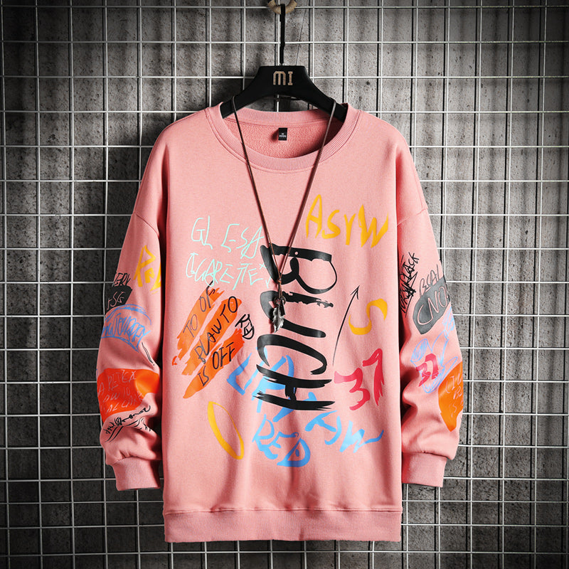 Pink sweatshirt with colorful text and graphics on a hanger against a tiled wall.