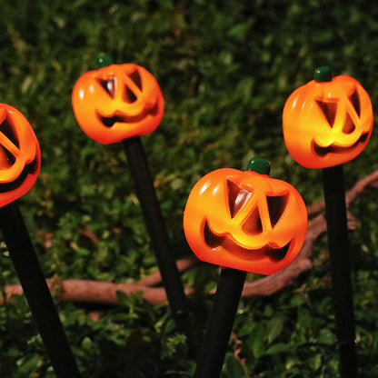 Orange pumpkin stake lights glowing among garden plants at night